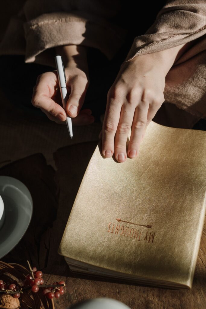 Close-up of hands writing in a gold-covered notebook with a pen on a wooden table.